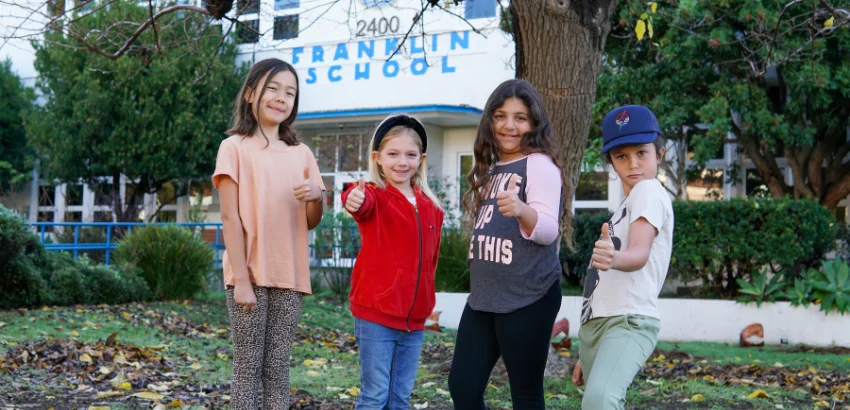 A group of children posing for a picture in front of a school.