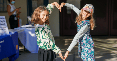 Two young girls making a heart with their hands.