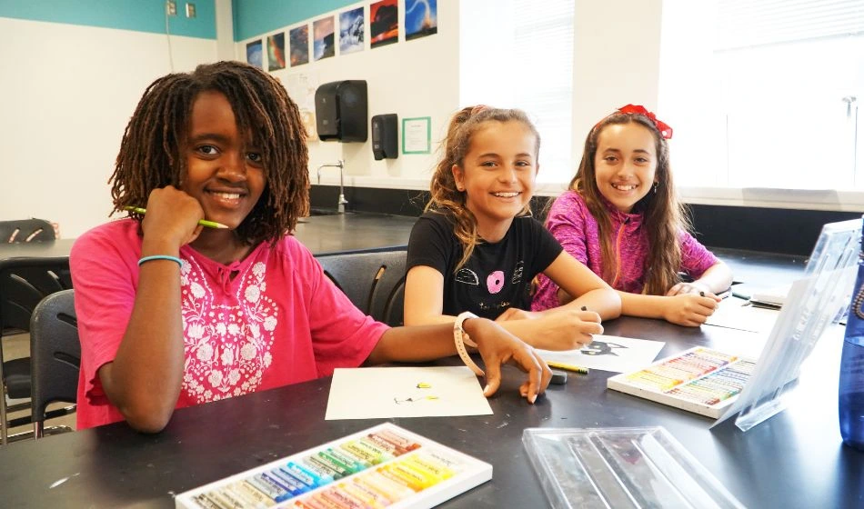 Three girls smile for a photo while working on an art project