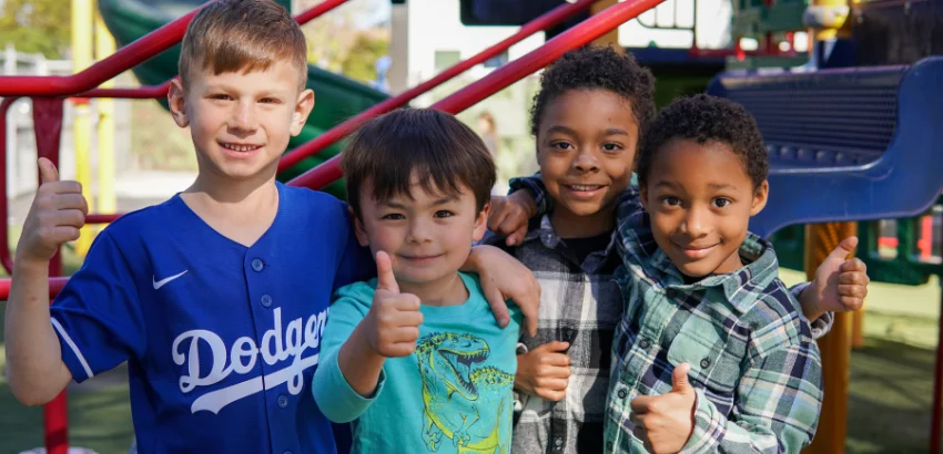 A group of boys giving thumbs up in a playground.