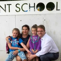 A family posing for a photo in front of a sign for a private school.