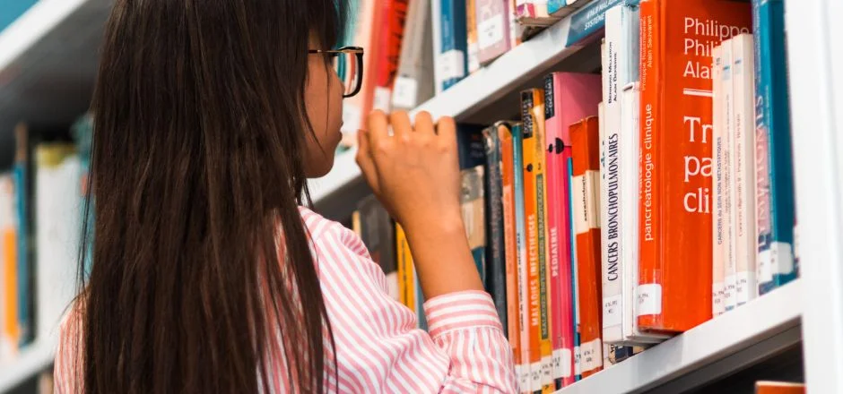 A young girl looks at books on a bookshelf