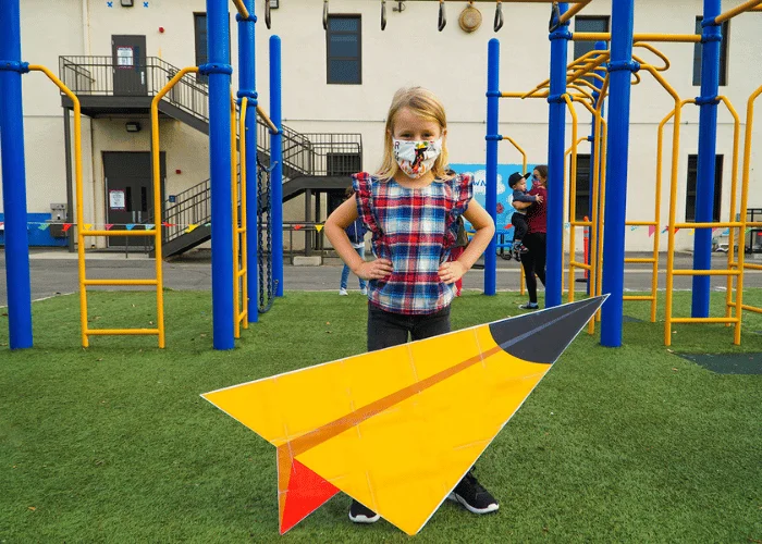 A girl wearing a face mask and holding a paper airplane.