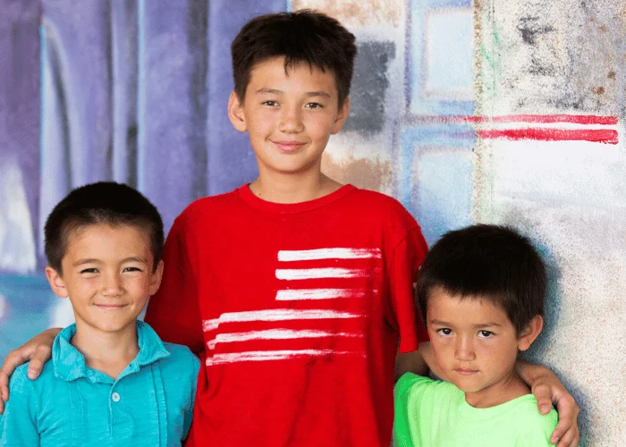 Three boys posing for a photo in front of a painting.