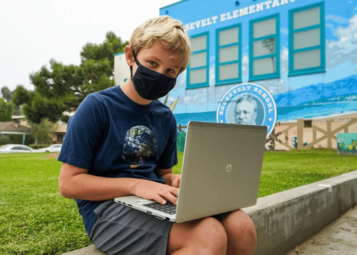 A boy wearing a face mask is using a laptop.