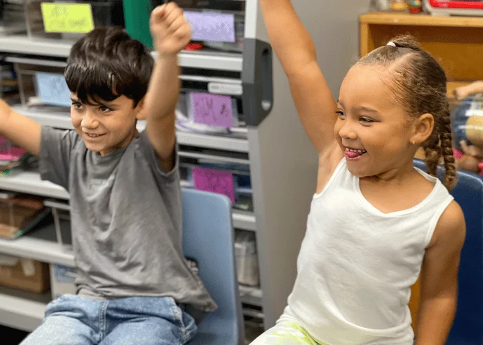 Two children sitting on chairs in a classroom.