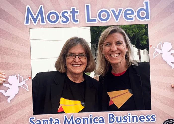 Two women standing in front of a sign that says most loved santa monica business.