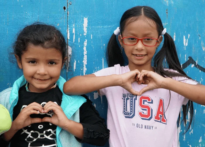 Three young girls make a heart sign in front of a blue wall.