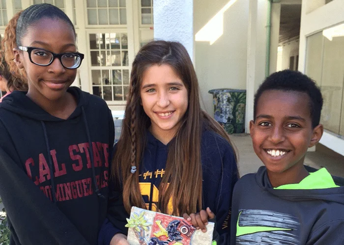 Three young people holding a book in front of a building.