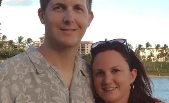 A man and woman posing for a photo in front of a body of water.