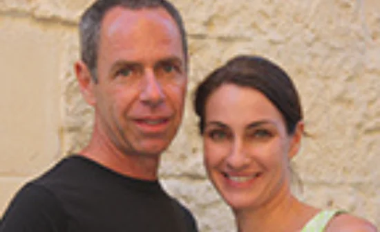 A man and woman posing in front of a stone wall.