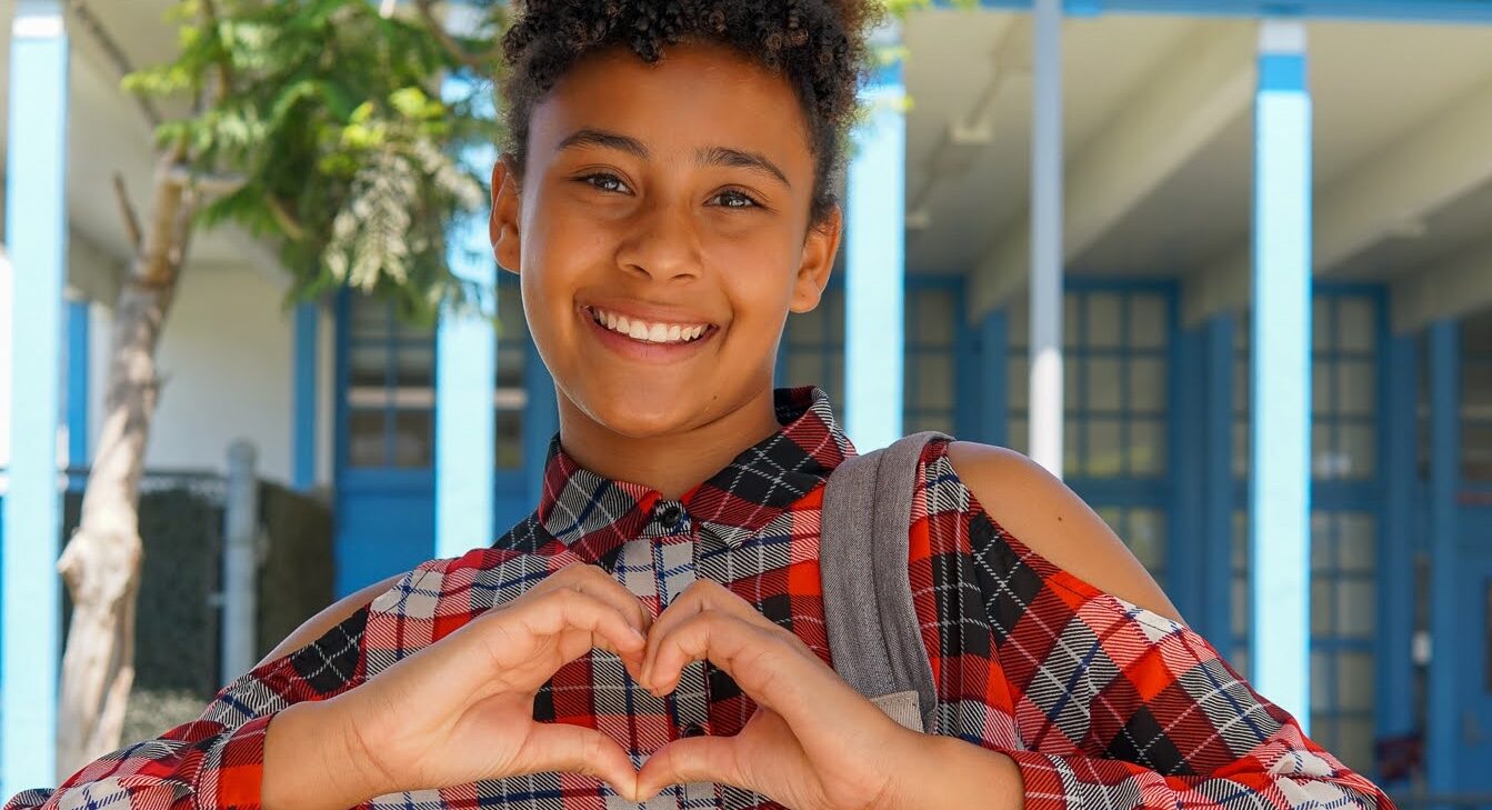 Two young girls making a heart with their hands.